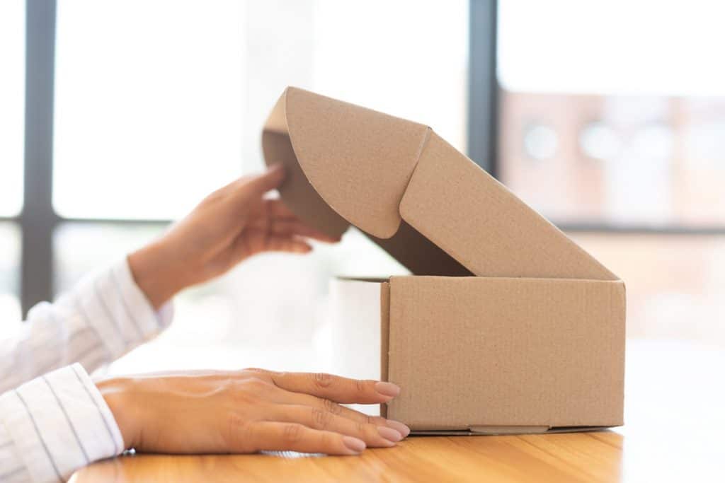 Delivery Service. Side view of lady unboxing her cardboard parcel on wooden desk, closeup