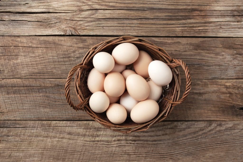 Organic chicken eggs in basket on wooden background. Organic household concept with eggs from free-range and pasture raised hens